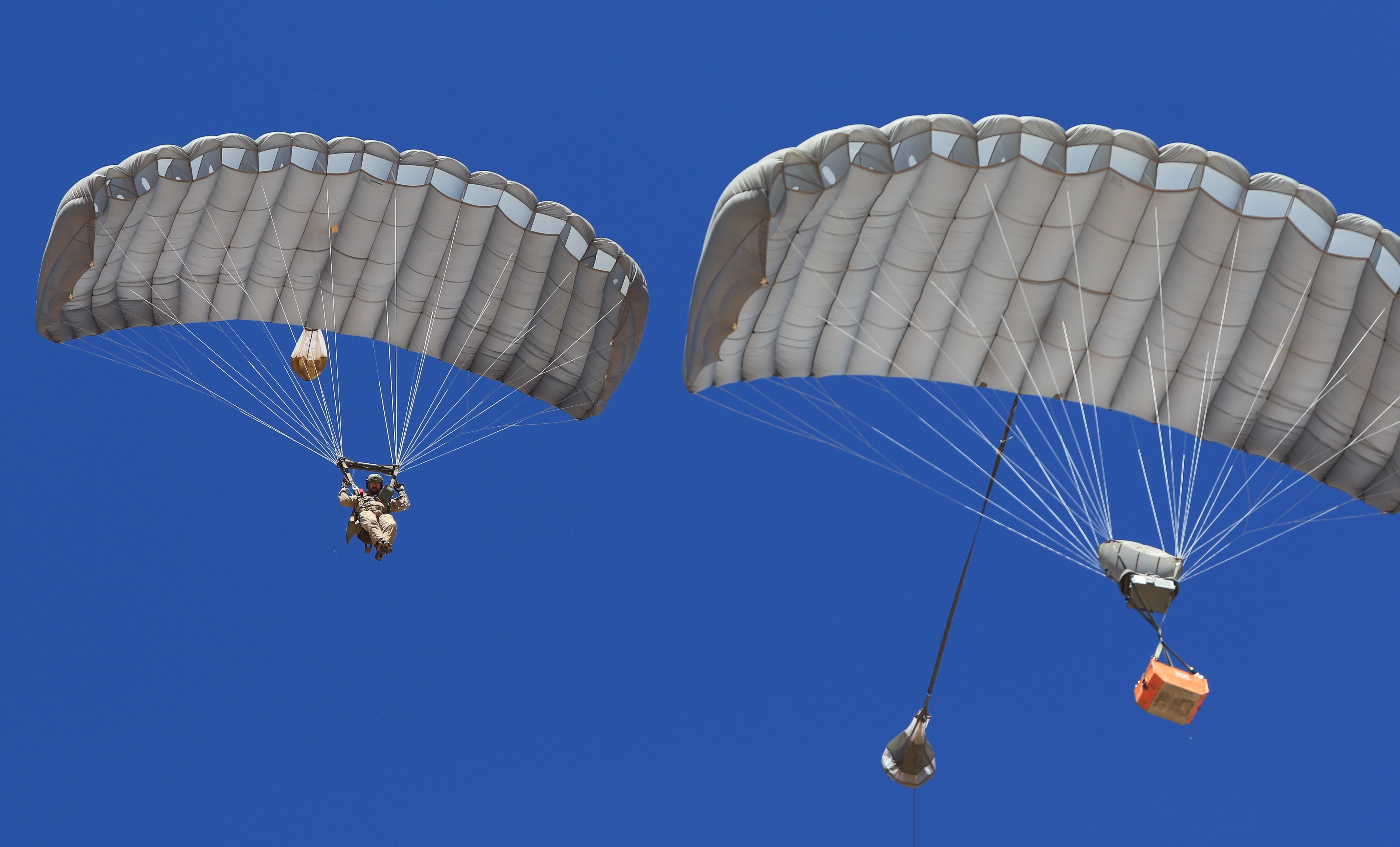 MicroFly II Military Army Cargo delivery system. JPADS / GPADS: Guided Precision Aerial Delivery System. Use with any Airborne Systems Ram Air Canopy. Soldier and orange cargo box with deployed canopies and blue sky.