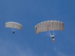 Airborne Systems Combo Drop MicroFly II Army Cargo delivery system. JPADS / GPADS: Guided Precision Aerial Delivery System. Use with any Airborne Systems Ram Air Canopy. Troop jumper and cargo parachute deployed canopy and blue sky.