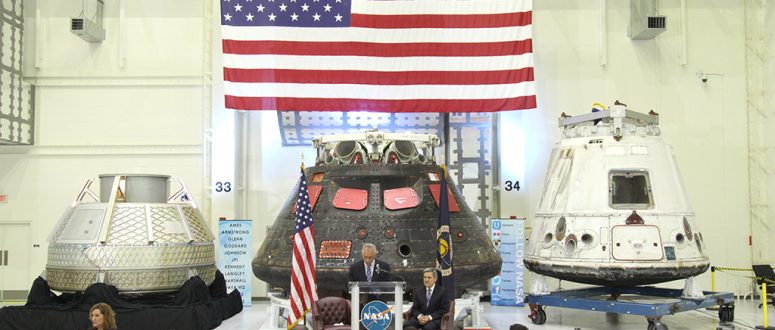 American Flag hanging above three space capsules. Seated crowd being addressed by NASA speakers. Airborne Systems. Design, development, and manufacture of space parachute & inflatable systems. Military-grade deceleration, airbag landing, aerospace recovery, personnel & cargo delivery parachute systems.