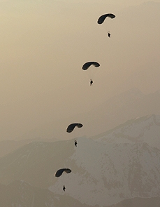 Airborne Systems - Intruder RA-1 Army Ram Air Parachute system for military special forces and beginner jumpers. Carries 450 lbs. Max deployment altitude 25,000 ft. 4 jumpers open canopies in formation, mountains snow hazy.