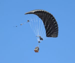 Airborne Systems FireFly Army Cargo Delivery Parachute System. JPADS 2K System of Choice. Carries unmanned loads up to 2,200 lbs. Max deployment altitude 24,500 ft. Canopy and cargo with blue sky.