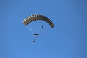 Airborne Systems - 2K1T Army cargo delivery parachute system. Low-cost canopy for one-time use. Drop loads up to 2,200 lbs. Max Deployment altitude 25,000 ft. Military cargo and canopy, blue sky.