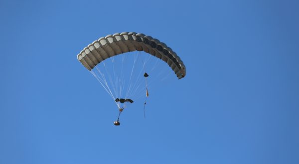 Airborne Systems - 2K1T Army cargo delivery parachute system. Low-cost canopy for one-time use. Drop loads up to 2,200 lbs. Max Deployment altitude 25,000 ft. Military cargo and canopy, blue sky.