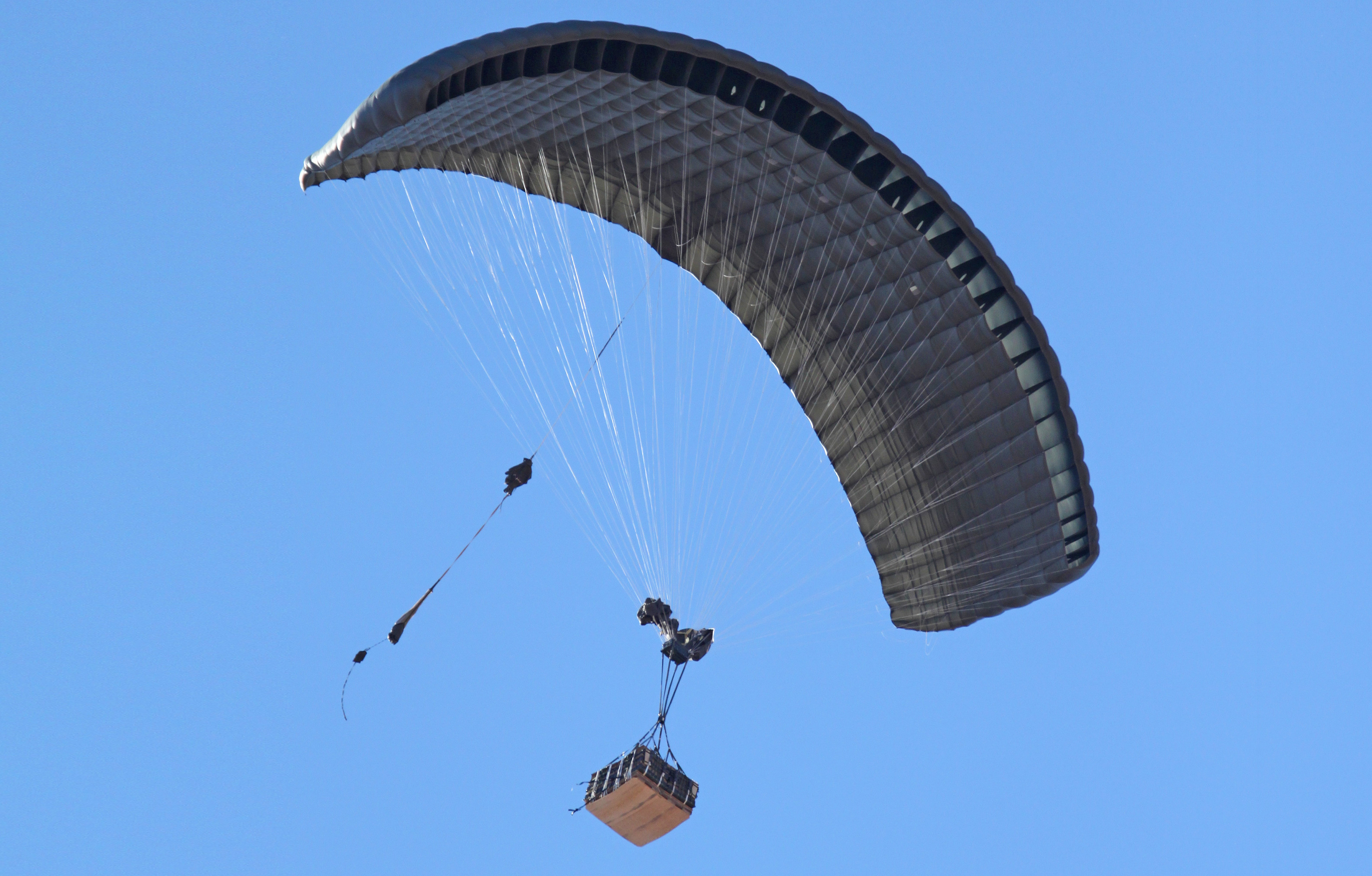 Airborne Systems - DragonFly Army Cargo Delivery Parachute System. JPADS 10K System of Choice. Eliptical canopy carries loads up to 10,000 lbs. Max altitude 24,500 ft. Military cargo and canopy, blue sky.