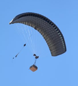 Airborne Systems - FireFly Army Cargo Delivery Parachute System. JPADS 2K System of Choice. Carries unmanned loads up to 2,200 lbs. Max deployment altitude 24,500 ft. Military cargo and inflated canopy from below, blue sky.