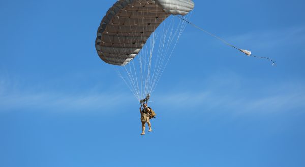 Airborne Systems - Hi-5 Army Military Ram Air Parachute Personnel product system for military special forces jumpers with glide modulation. Carries 485 lbs. Max deployment altitude 25,000 feet. Paratrooper deployed parachute blue sky.