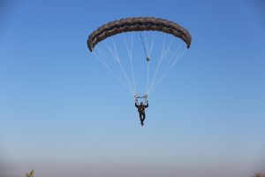 Airborne Systems - Hi-5 Army Military Ram Air Parachute Personnel product system for military special forces jumpers with glide modulation. Carries 485 lbs. Max deployment altitude 25,000 feet. Paratrooper deployed parachute blue sky.