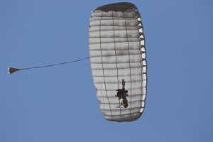 Airborne Systems - Hi-5 Army Military Ram Air Parachute Personnel product system for military special forces jumpers with glide modulation. Carries 485 lbs. Max deployment altitude 25,000 feet. Paratrooper deployed parachute from below, blue sky.