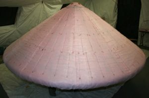 Airborne Systems Hypersonic Inflatable Aerodynamic Decelerators (HIAD) inflatable heat shield for re-entry of spacecraft into Earth and Mars. Inflatable space parachutes. Design, development, and manufacture of inflatable parachute systems for aerospace structures used by the military and NASA. Pink pyramid-cone-shaped inflated SIAD.