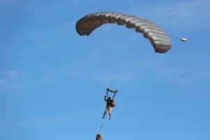 Airborne Systems - MMS Multi-mission Army Ram Air Parachute system for military special forces jumpers. Carries 450-485 lbs. Max deployment altitude 25,000 ft. Jumper and Ram Air canopy, blue sky.
