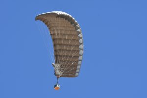 Airborne Systems - FlyClops Army Cargo delivery parachute: one-time use GPADS / JPADS. Carries payloads from 750-2200 lbs. Max deployment altitude 17,500 ft. Military cargo and canopy from below, blue sky.