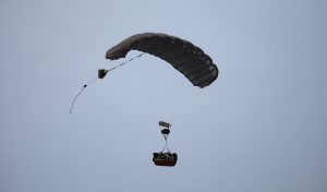 Airborne Systems JPADS and GPADS training courses for military parachute cargo drop missions, army navigation systems for jumpers, and guided precision aerial delivery systems. Deployed canopy with cargo and grey sky.