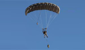 Airborne Systems Hi-5 Army Ram Air Parachute system for military special forces jumpers with glide modulation. Carries 485 lbs. Max deployment altitude 25,000 ft. Deployed canopy and jumper with blue sky.