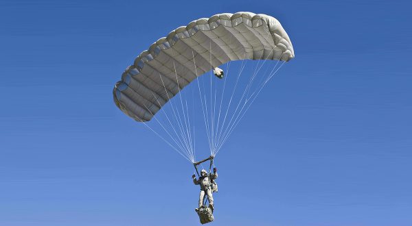 Airborne Systems Intruder RA-1 Army Ram Air Parachute system for military special forces and beginner jumpers. Carries 450 lbs. Max deployment altitude 25,000 ft. Deployed canopy with military jumper / gear bag and blue sky.
