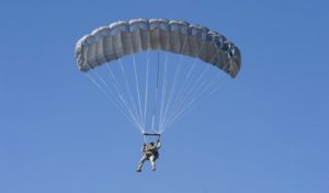 Airborne Systems Intruder RA-1 Army Ram Air Parachute system for military special forces and beginner jumpers. Carries 450 lbs. Max deployment altitude 25,000 ft. Deployed canopy with military jumper and blue sky.