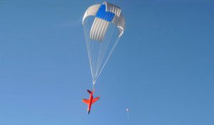 Airborne Systems Military & space textile manufacturing & design. Army & space parachute canopies, aerial delivery (GPADS/JPADS). Aircraft & spacecraft deceleration systems. Orange aircraft full descent dragging blue and white deceleration canopy.