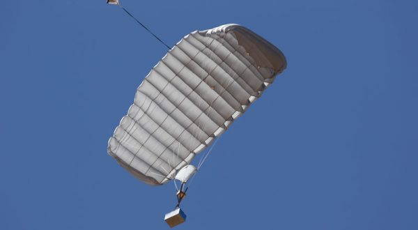 Airborne Systems Canopy with payload. FC Mini Army cargo delivery parachute system. JPADS / GPADS: Guided Precision Aerial Delivery System. Carries 200-500 lbs. Max deployment altitude 24,500 ft. Deployed canopy with blue cargo box and blue sky.