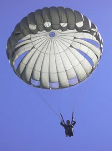 Airborne Systems MC-6 Army Troop Parachute non-steerable for military jumpers. Low opening. Carries up to 400 lbs. Minimum deployment altitude 500 ft. lone soldier with blue sky.