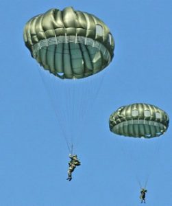 Airborne Systems MC-6 Army Troop Parachute non-steerable for military jumpers. Low opening. Carries up to 400 lbs. Minimum deployment altitude 500 ft. Two soldiers, green canopies and blue sky.