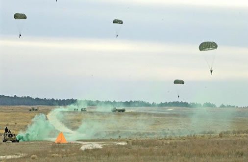 Airborne Systems MC-6 Army Troop Parachute non-steerable for military jumpers. Low opening. Carries up to 400 lbs. Minimum deployment altitude 500 ft. Desert landing five parachutes. Jeep in foreground.