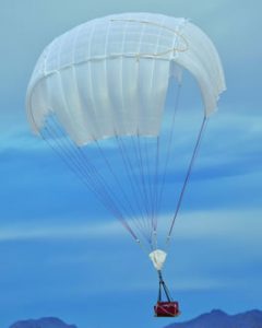 Airborne Systems Unicross Army cargo delivery parachute system. Low cost, modular design for one-time use or quick repack. Three sizes carry payloads of 75 lbs to 3,200 lbs. Cargo drop deployed white canopy and red cargo box with blue sky and mountains behind.