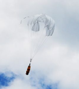 Airborne Systems Unicross Army cargo delivery parachute system. Low cost, modular design for one-time use or quick repack. Three sizes carry payloads of 75 lbs to 3,200 lbs. Cargo drop with deployed canopy and cloudy blue sky.