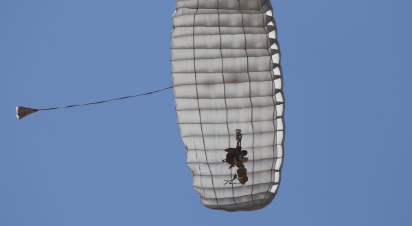 Airborne Systems Hi-5 Army Ram Air Parachute Personnel product system for military special forces jumpers with glide modulation. Carries 485 lbs. Max deployment altitude 25,000 feet. Deployed canopy and parachutist from below with blue sky.